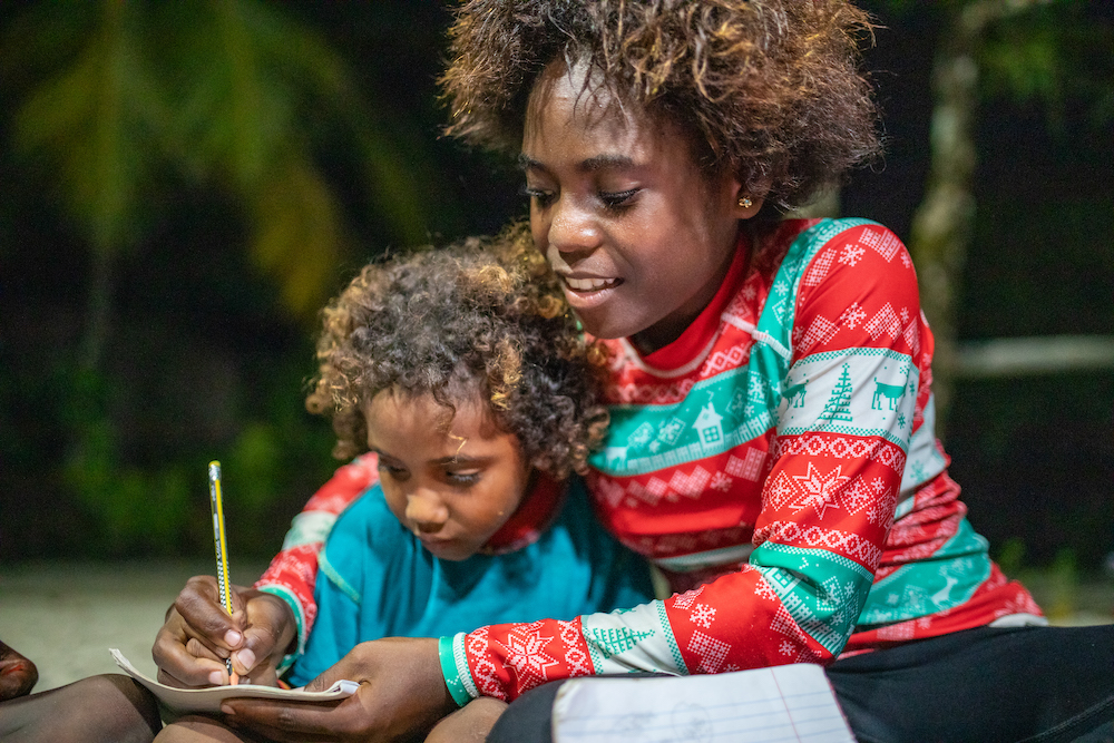Young woman helping a child to write under the solar light.