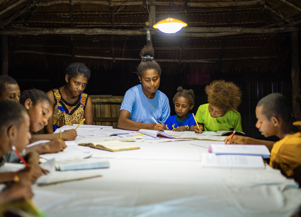 Family studying around a table at night using a solar powered light